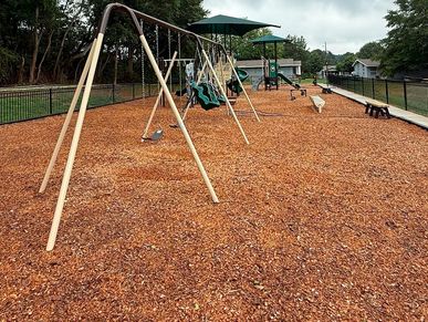 Empty playground with swings and wood chip ground covering.