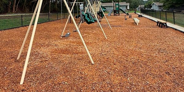 Empty playground swings over wood chip ground covering.