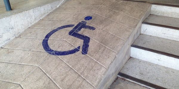 Concrete wheelchair ramp with accessibility symbol beside stairs.