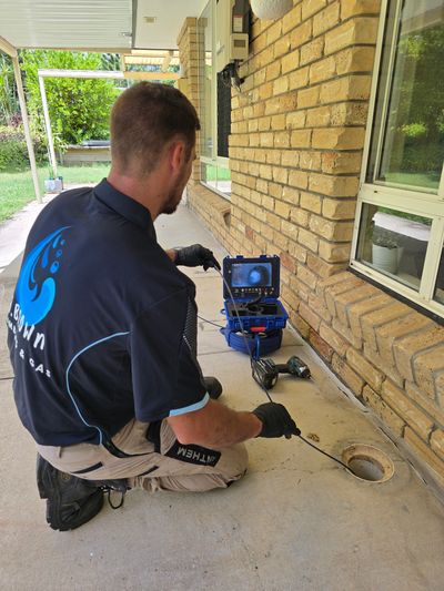 Technician using a camera inspection tool on a drain outside a brick house.