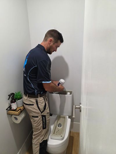 A plumber repairing a toilet tank inside a small bathroom.