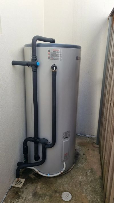 A water heater with black insulated pipes in a small outdoor corner.