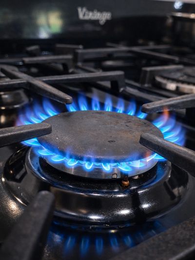 Blue flames burning on a gas stove burner in a kitchen.