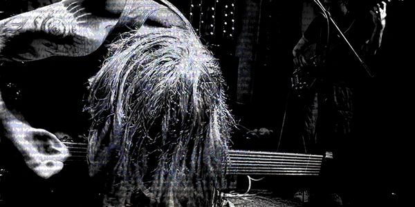 A tattooed musician intensely playing guitar on stage with dramatic lighting.