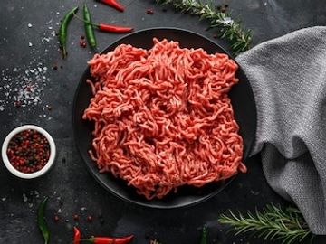 Lean and tender Minced Beef on plate with seasoning scattered on the table. Born & reared in Malpas.