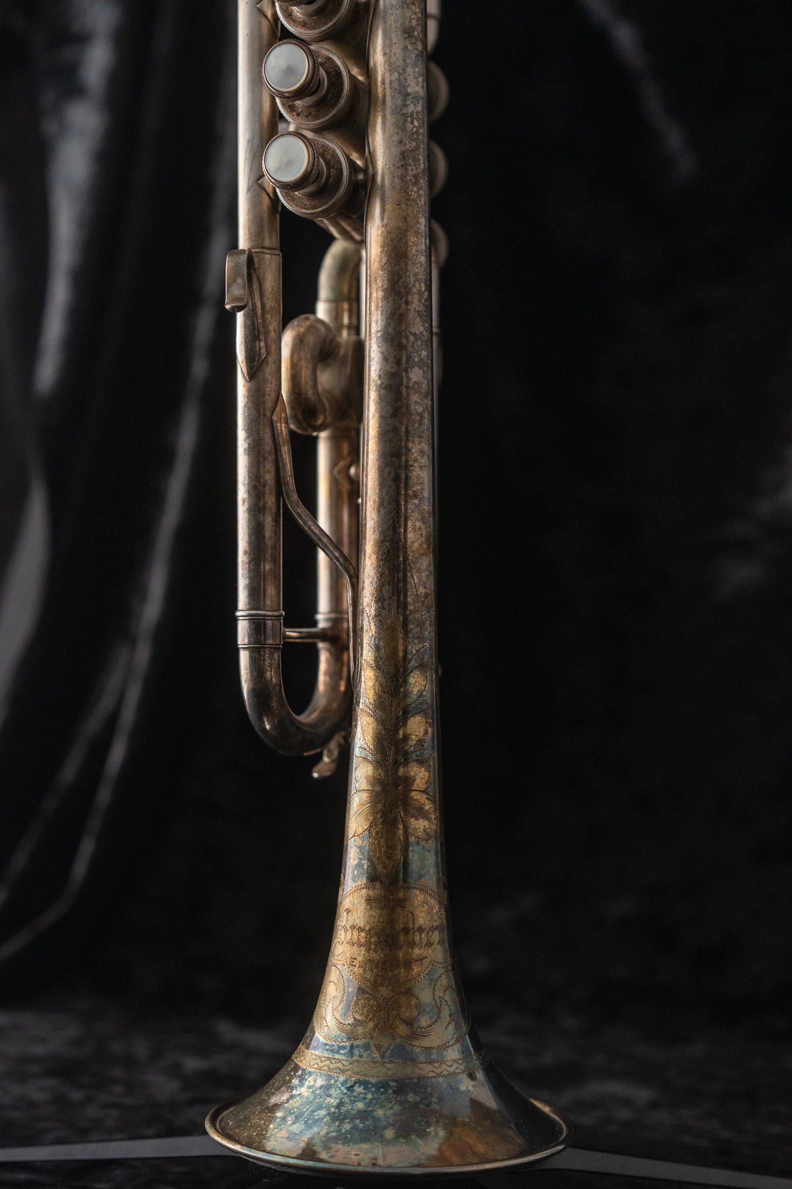 Close-up of an antique trumpet with detailed engravings against a dark background.