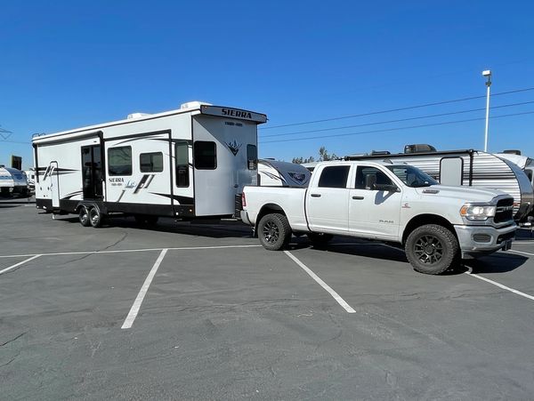 White pickup truck towing a large Sierra RV in parking lot.