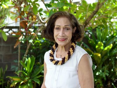 Smiling woman outdoors with a floral necklace.