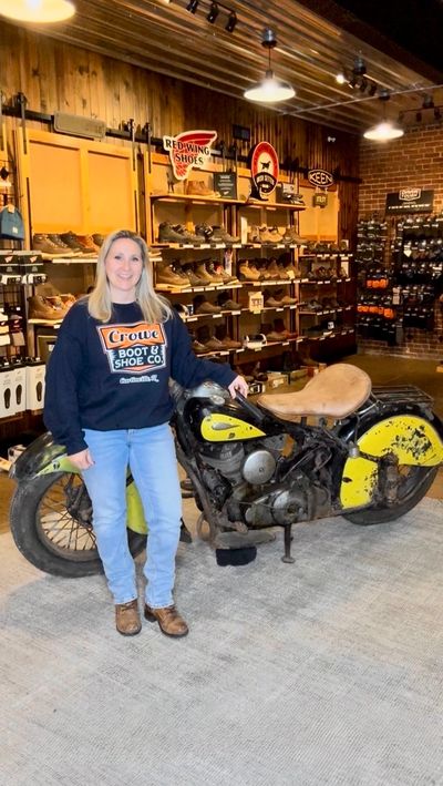 Woman posing with vintage motorcycle inside a shoe store.