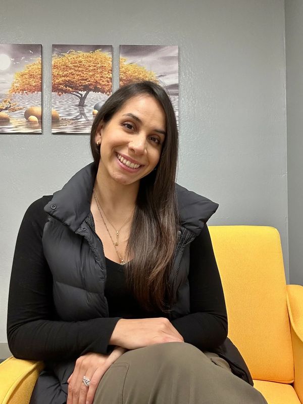 Woman sitting on a yellow chair, smiling warmly.