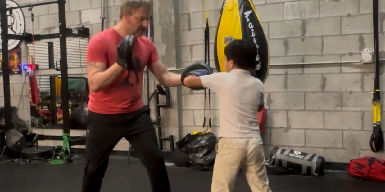 Man training a young boy in boxing with gloves in a gym.