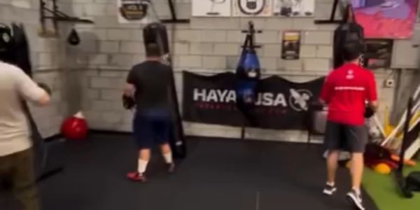Three people training in a gym with punching bags.