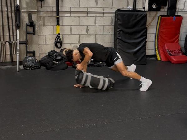 Man performing a push-up with a weighted sandbag in a gym.