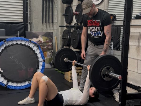 Woman lifting weights with trainer spotting her in a gym.