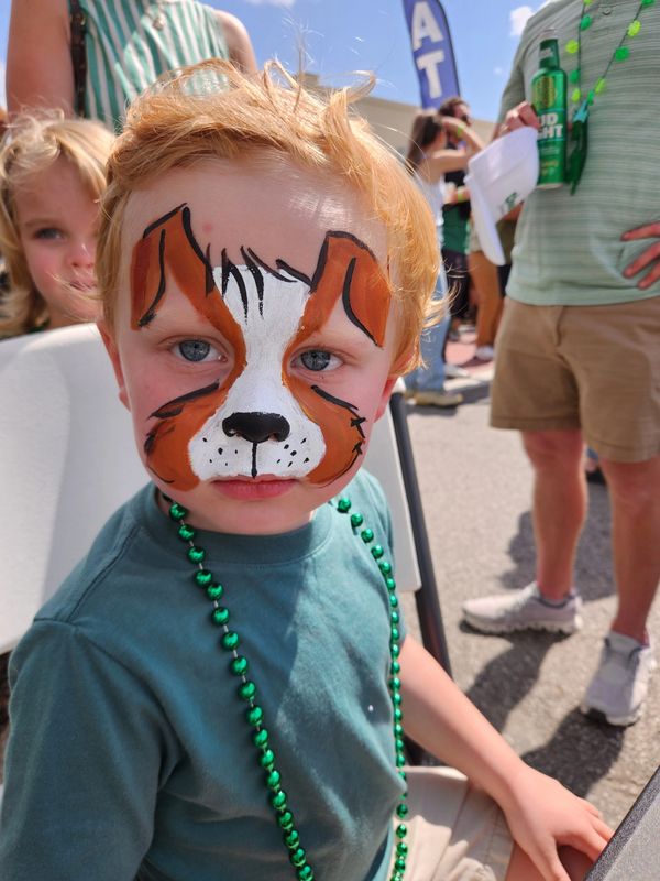 Young boy with dog face paint and green beads at an outdoor event.