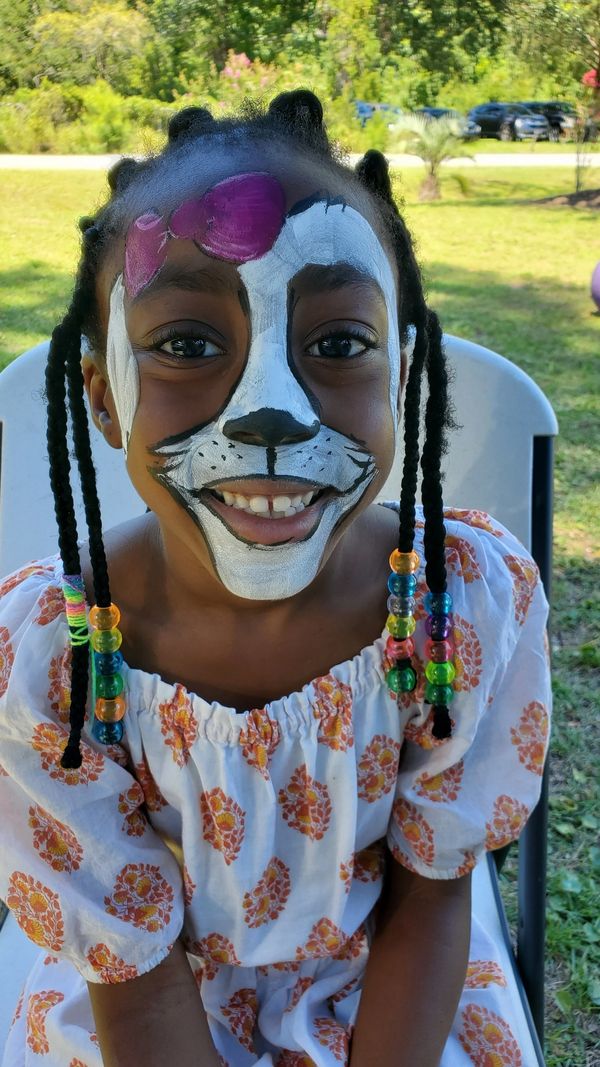 Smiling girl with colorful beads and face paint of a white cat with a pink bow.