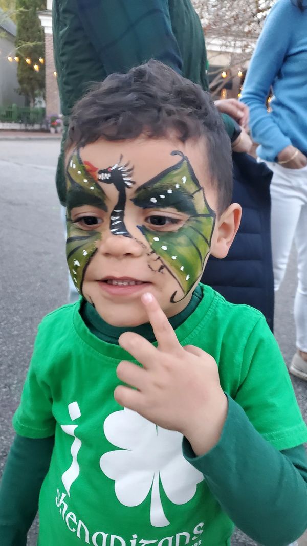 A child with dragon face paint pointing to their cheek.