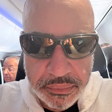 Man with sunglasses taking a selfie on an airplane.