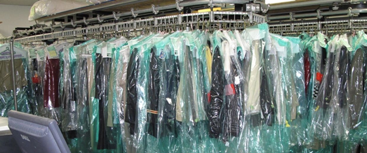 Clothes covered in plastic hanging on a rack at a dry cleaner.
