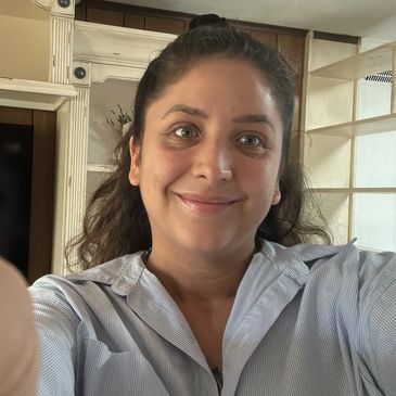 A woman smiling indoors, taking a selfie.