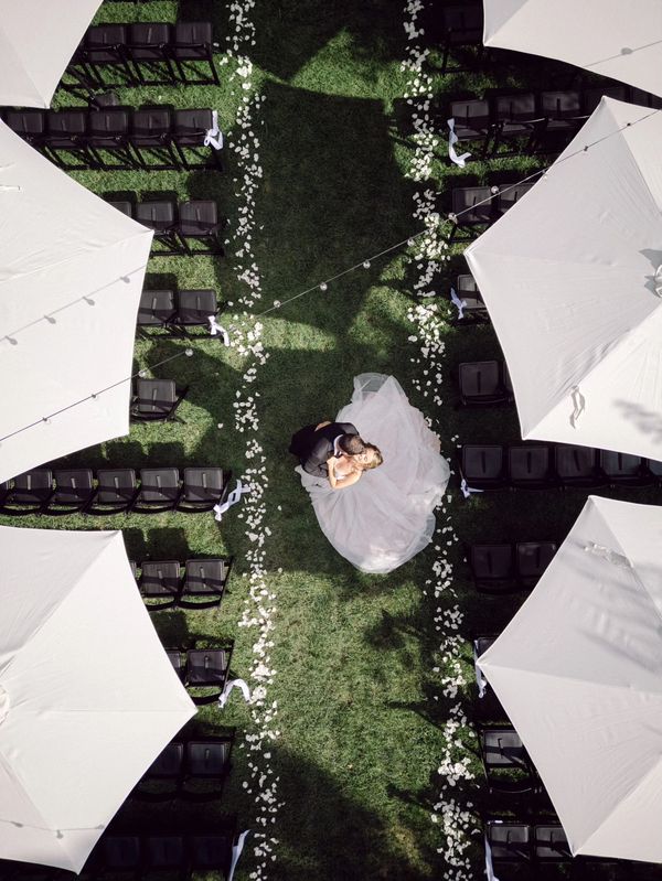 outdoor ceremony drone shot. umbrellas, rose petal aisle, bride and groom, string lights