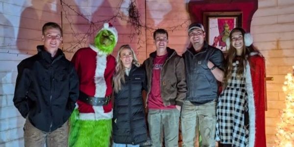 Group photo with a person dressed as the Grinch and festive holiday decorations at night.