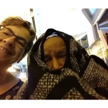 Two people smiling, one wrapped in a patterned blanket.