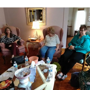 Three women sitting in a living room around a coffee table with water bottles.