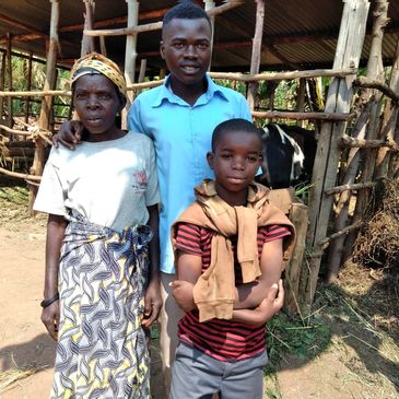 Three people standing outdoors near a wooden animal enclosure with a cow inside.