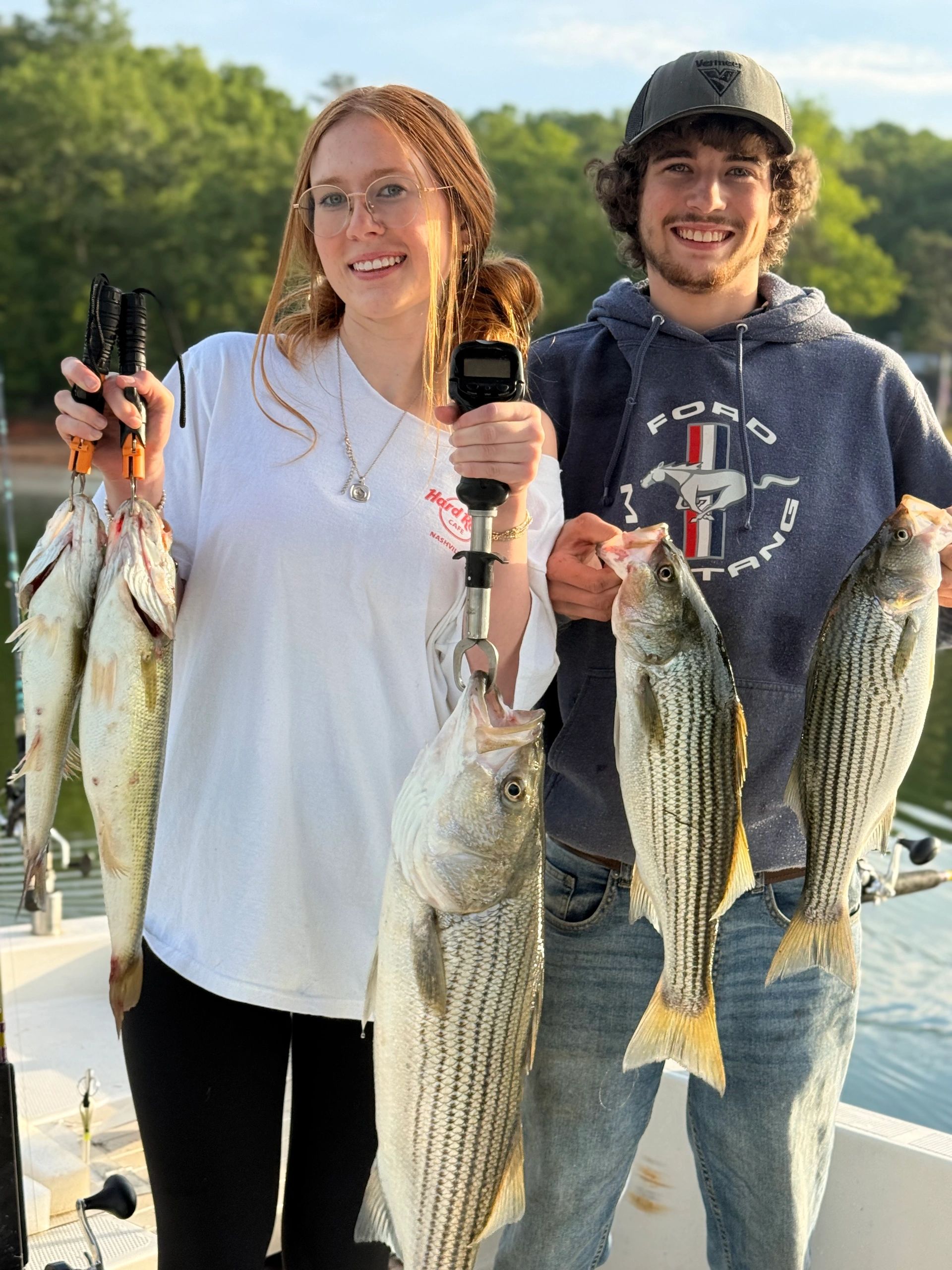 Two smiling people proudly holding several freshly caught fish outdoors.