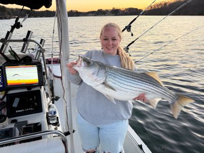 Woman on boat holding a large fish at sunset.