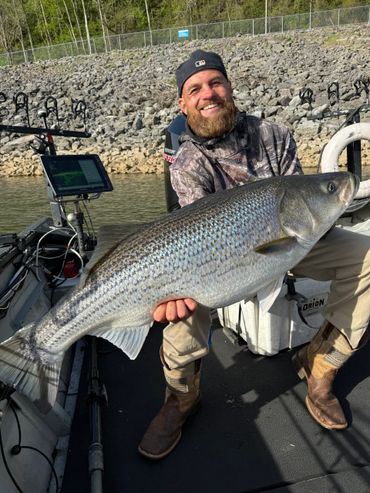 Man holding a large striped bass on a boat, smiling.