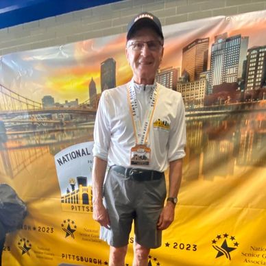 Elderly man proudly wearing a medal at a Pittsburgh event backdrop.