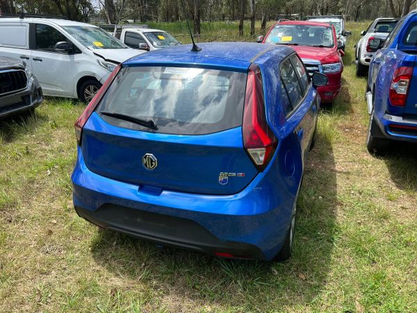 Blue MG electric car parked on grass with other vehicles around.
