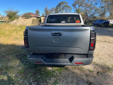 Rear view of a silver pickup truck parked on a gravel surface.