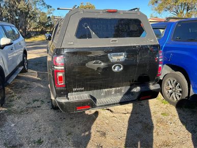 A black Great Wall pickup truck parked between two other vehicles on a gravel surface.