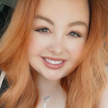 A smiling woman with red hair and a silver necklace.