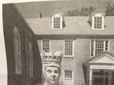Statue of a crowned figure in front of a historic building.