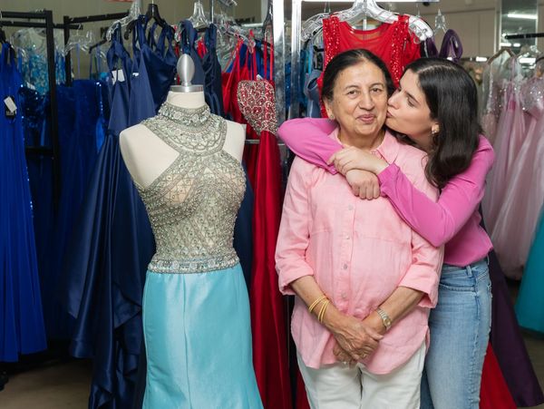 A young woman hugs and kisses an older woman in a dress shop.