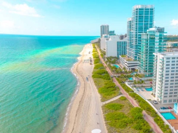 Aerial view of a sunny beach with turquoise water and beachfront buildings.