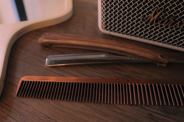 A wooden comb and straight razor on a wooden surface near a Marshall speaker.