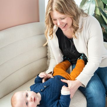 Smiling woman playing with a baby on a couch.
