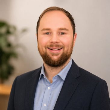 Smiling man in a suit with a beard against a blurred background.