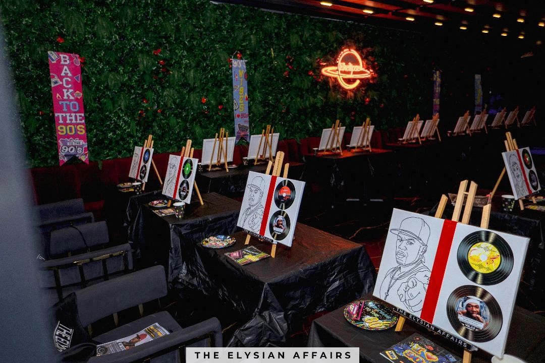 Art easels with 90s-themed paintings set up in a dimly lit room.