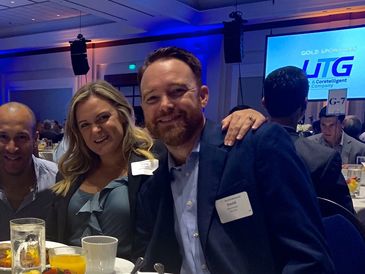 Smiling man in a suit at a formal event with a woman beside him.