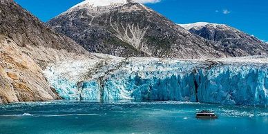 A boat near a massive blue glacier with snow-capped mountains.
