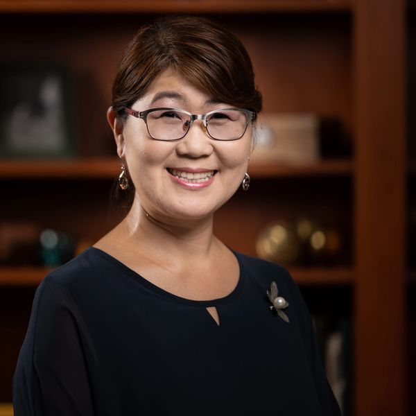 Smiling woman with glasses in a dark blouse poses in a warmly lit room.