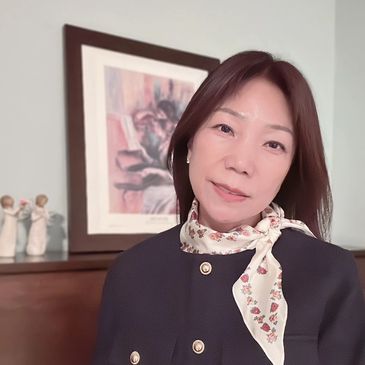 A woman with a floral scarf poses indoors by a framed artwork.