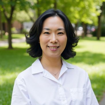 Smiling woman in white shirt outdoors with green trees background.