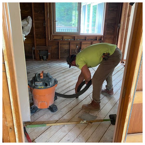 Man cleaning up after full gut demolition job. Using shop vac to extract dust from debris.